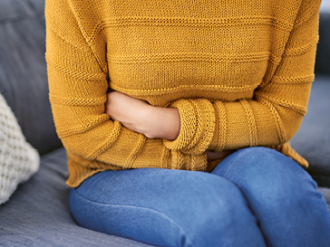 Frau in orangenem Pullover hält sich die Arme an den Bauch.