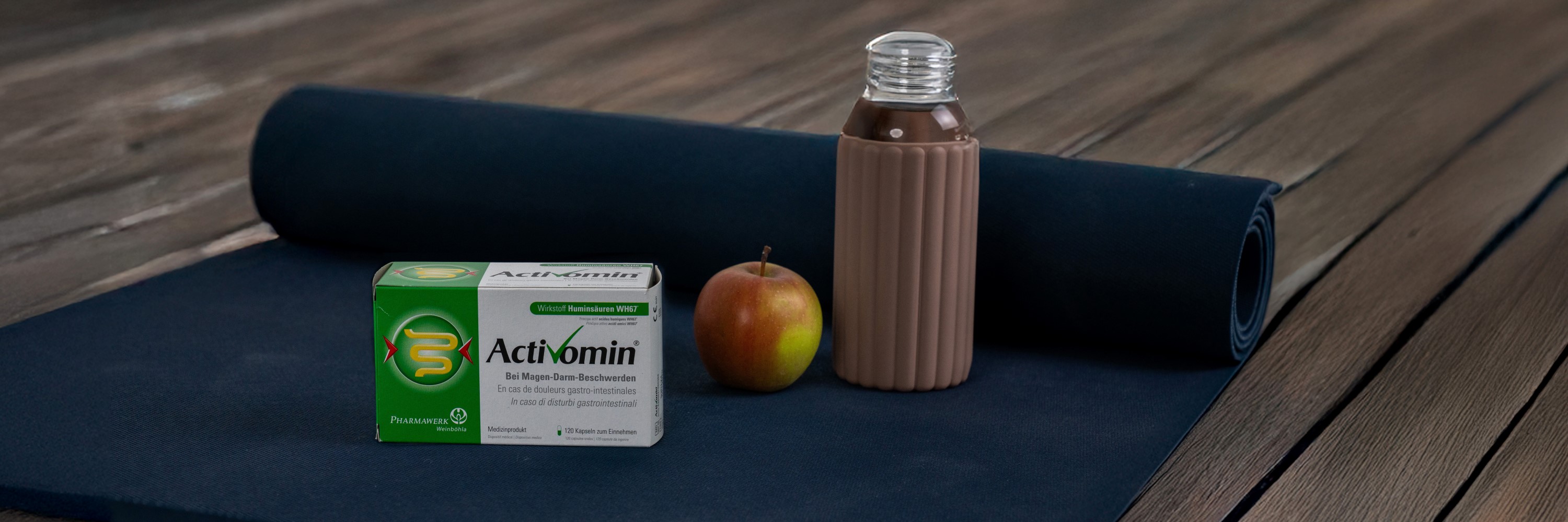 Apfel, Wasserflasche und Activomin-Schachtel stehen auf einer blauen Yoga-Matte.